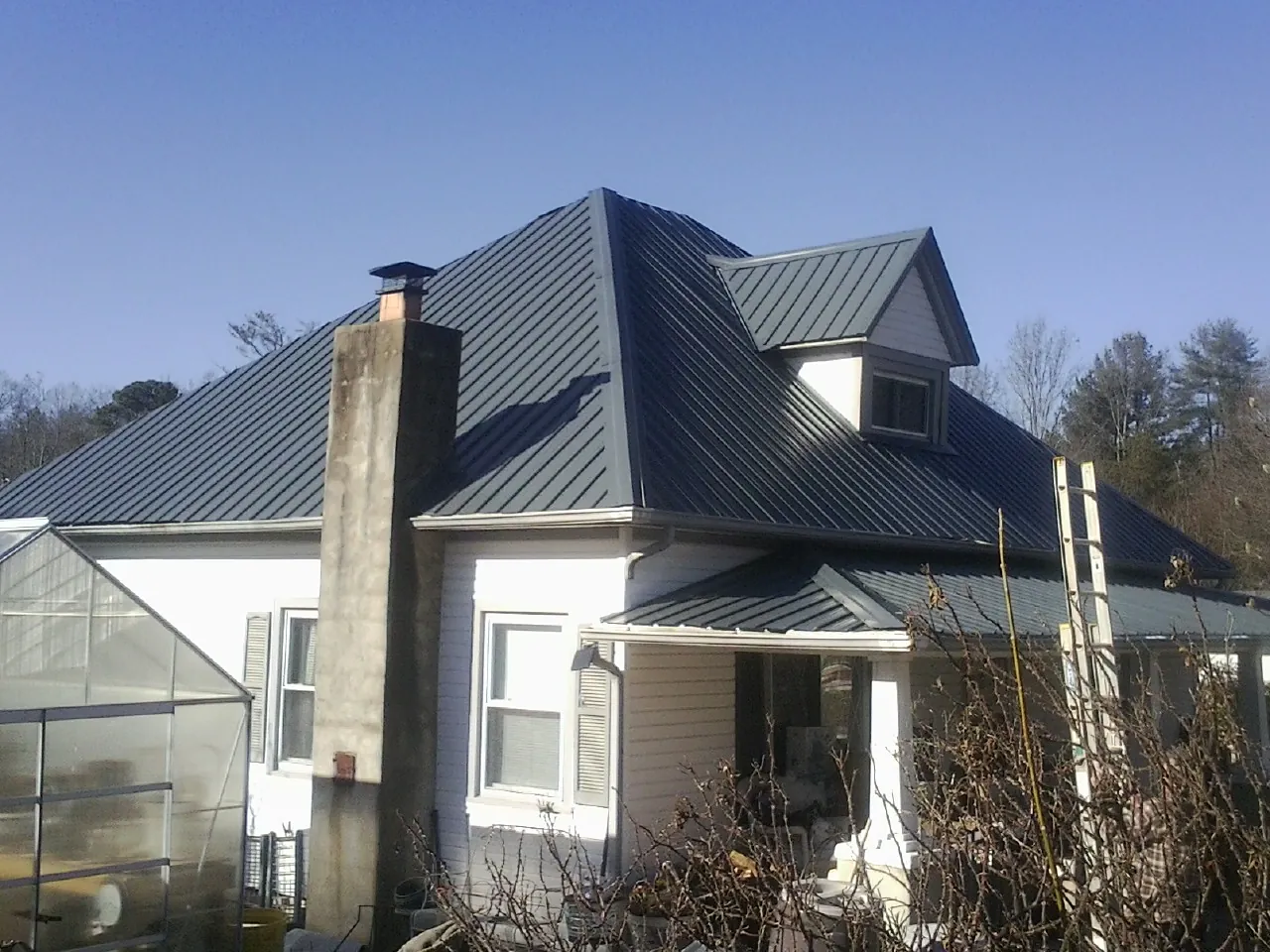 Dark blue standing seam metal roof on a white farmhouse with dormer — Slate & Tile Roof Repair by Roofing Brothers in Tafton