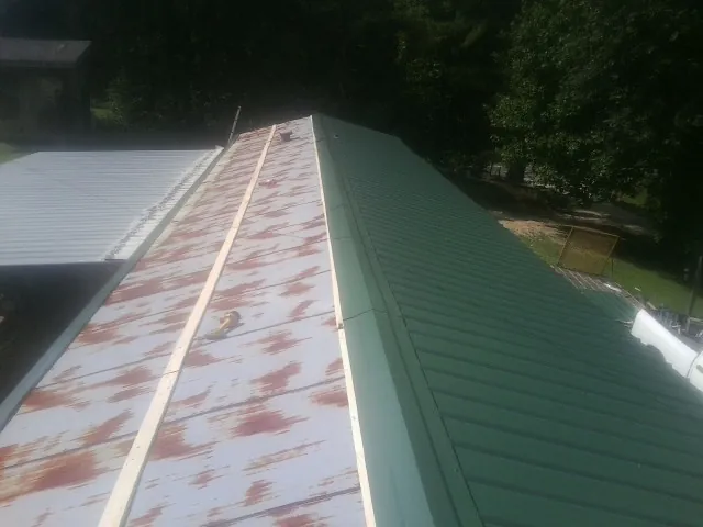Old rusted panels beside newly installed green metal roofing — Wind Damage Roof Repair by Roofing Brothers in Tafton