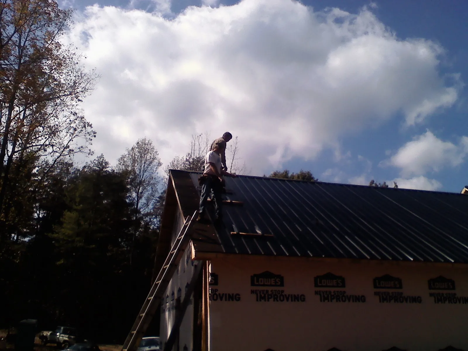 Roofer fastening dark metal panels high against a cloudy sky, from a Roof Inspection job in Tafton