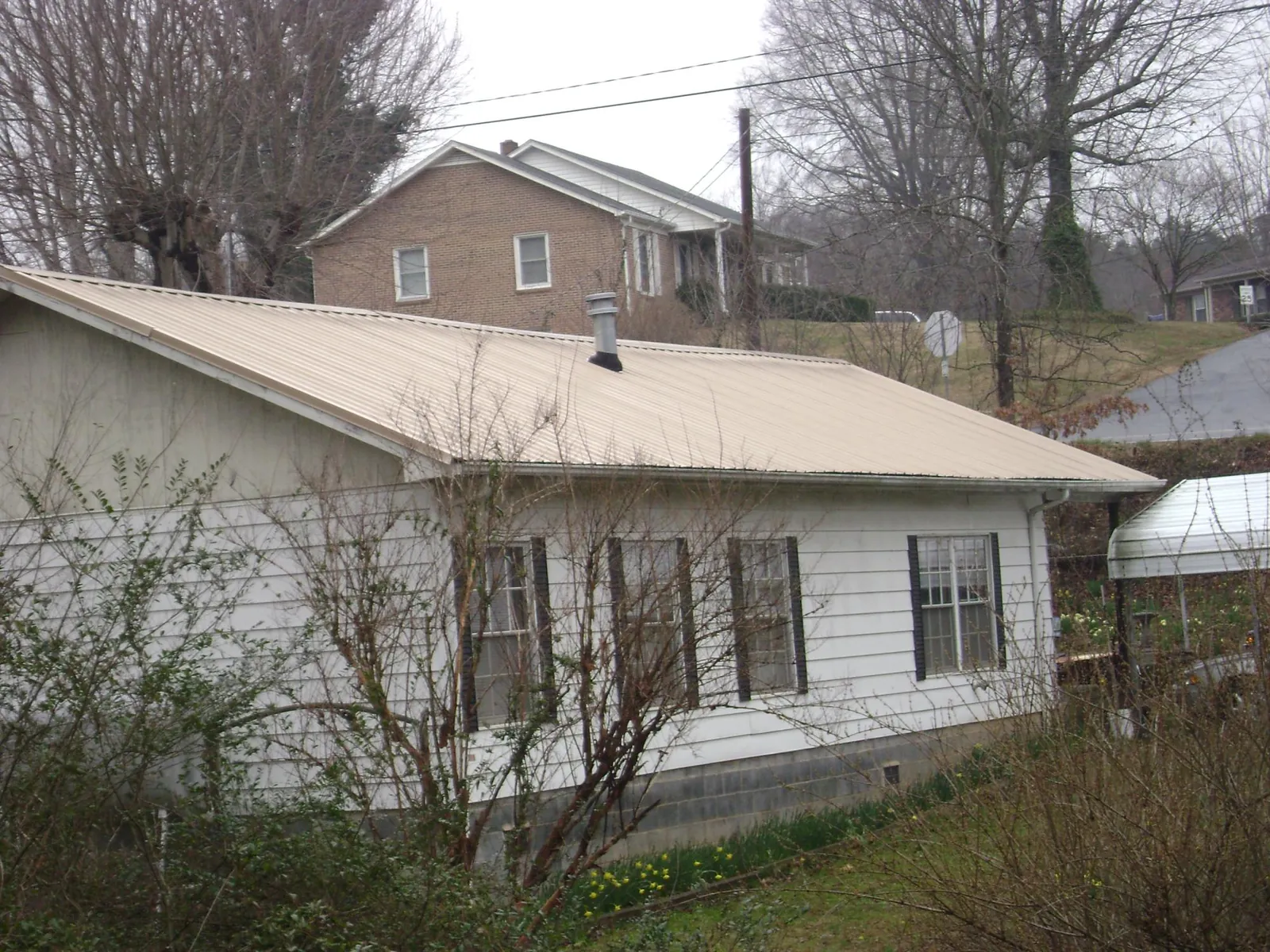Tan metal roof on a white sided house set into a hillside — Commercial Roofing by Roofing Brothers in Tafton
