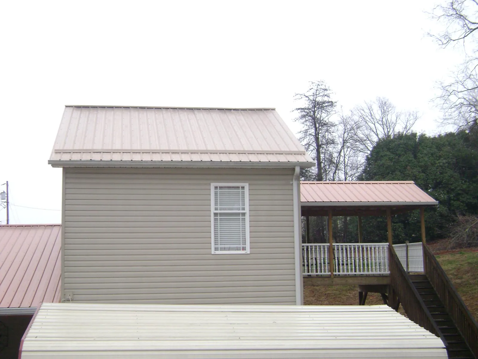 Tan metal roofs on a two story addition and attached porch, from a Roof Replacement job in Tafton